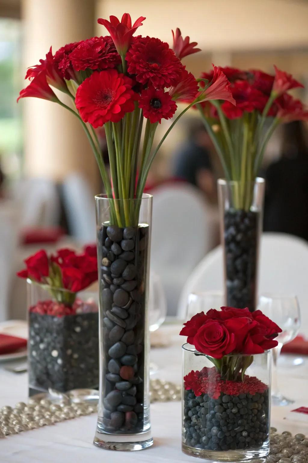 Vases of varying heights filled with red flowers and black stones for depth.