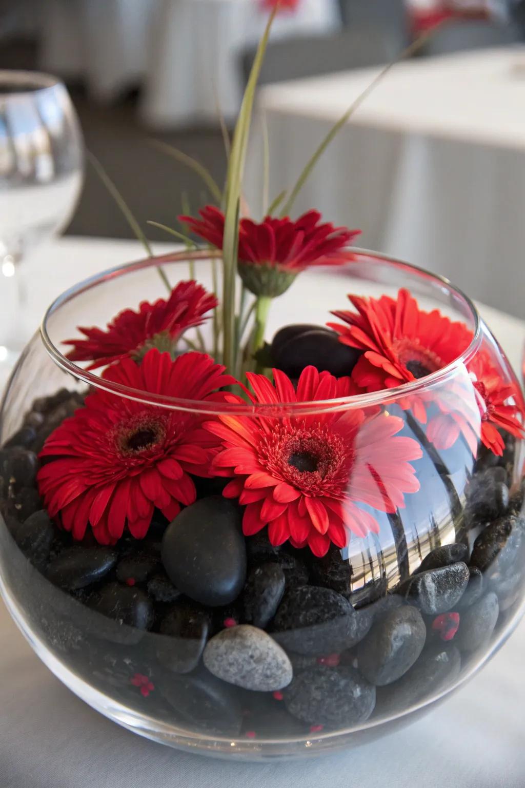 Floating red flowers over black stones in a glass bowl for a serene centerpiece.