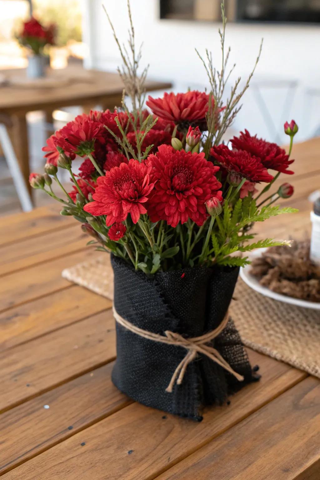 A rustic centerpiece featuring red blooms wrapped in black burlap.